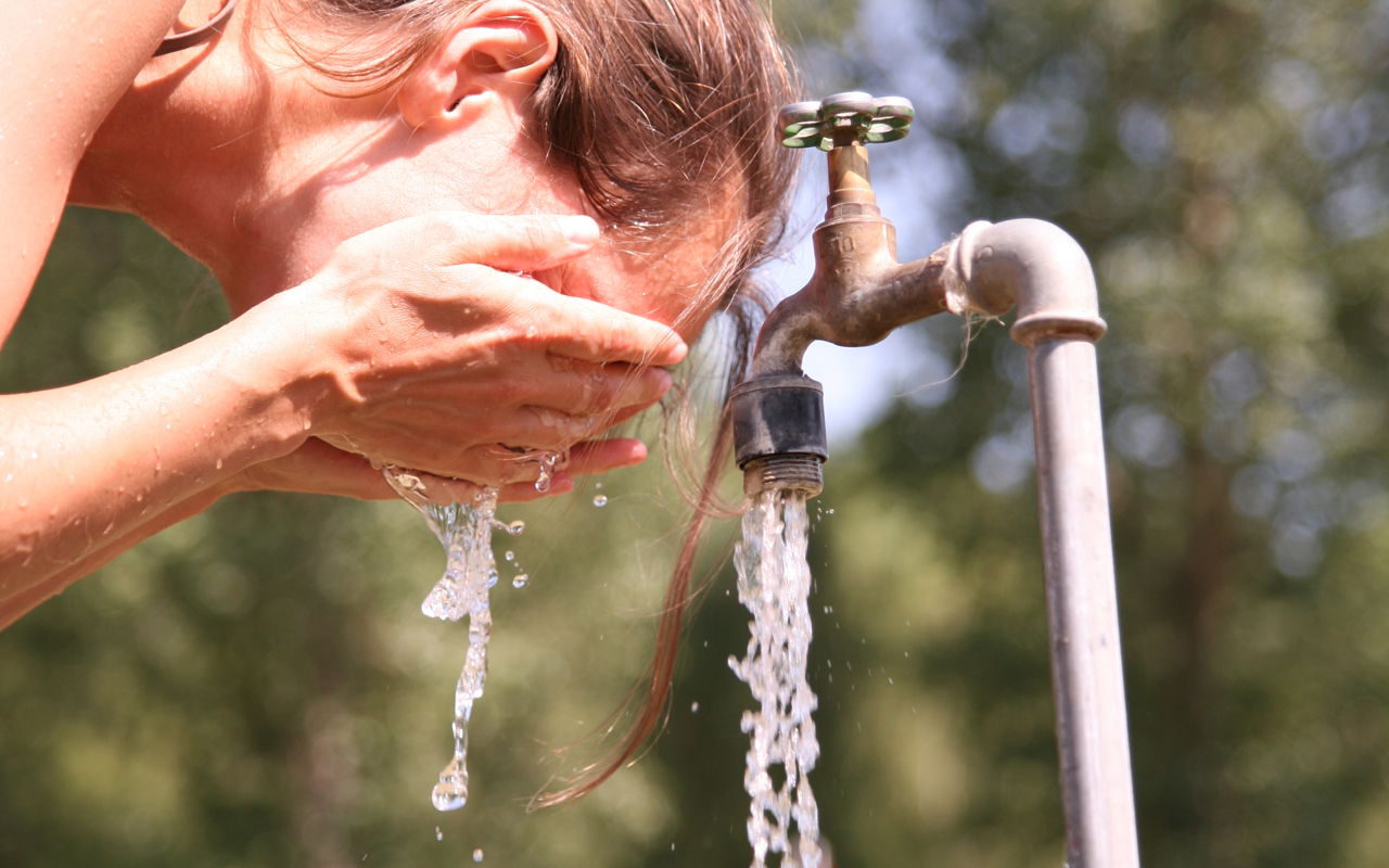 Kvinde vasker sig ansigt ved en udendørs vandhane