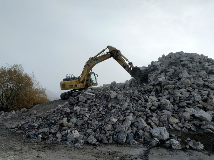 Et bjerg af nedknust beton med en gravemaskine på toppen.
