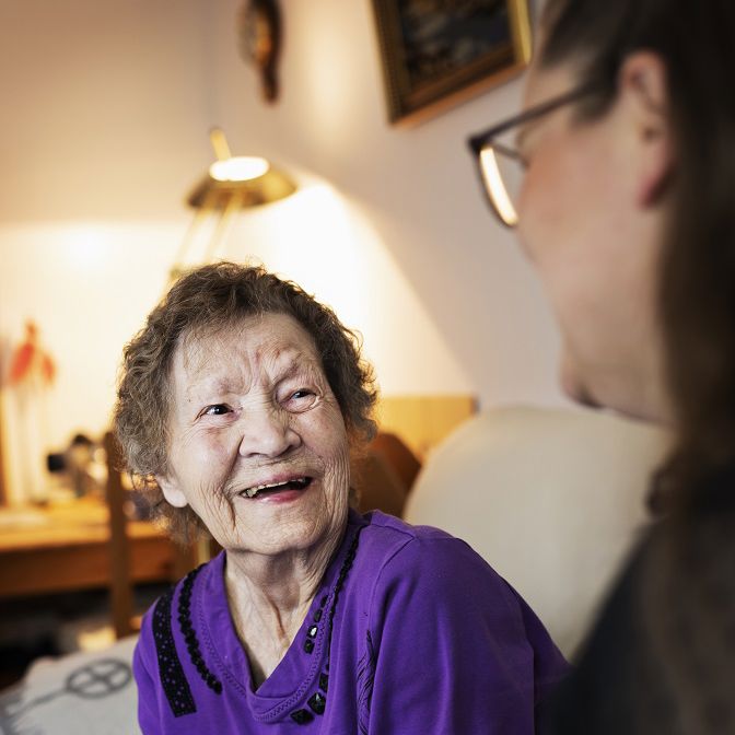 Ældre dame griner. Hun snakker med en SOSU-hjælper.